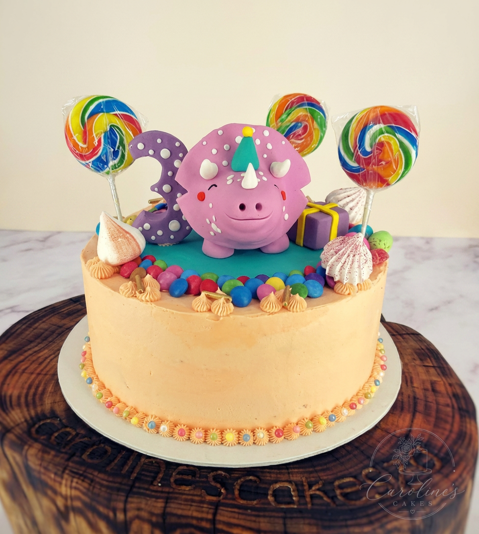 Peach buttercream cake with pink dragon, lollipops and sweets