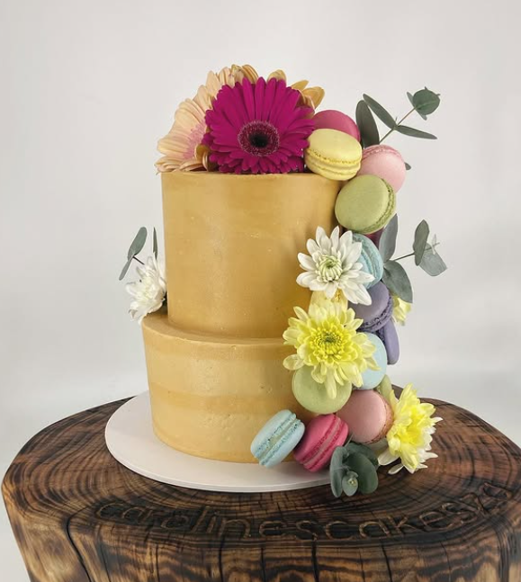 Two-tier gold buttercream cake cascading with macarons and gerberas